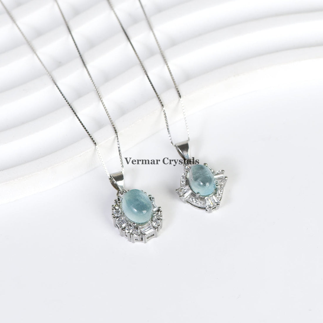 Elegant silver necklace with oval aquamarine blue pendant surrounded by sparkling stones on white background