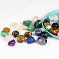 Collection of polished colorful tumblestones including rose quartz, amethyst, tiger’s eye, green aventurine, and lapis lazuli on white background