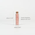 Glass vial filled with small pink crystal chips sealed with natural cork on white background with measurements