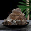 Pile of natural smoky quartz crystal stones with rough translucent brown and gray surfaces on a black plate