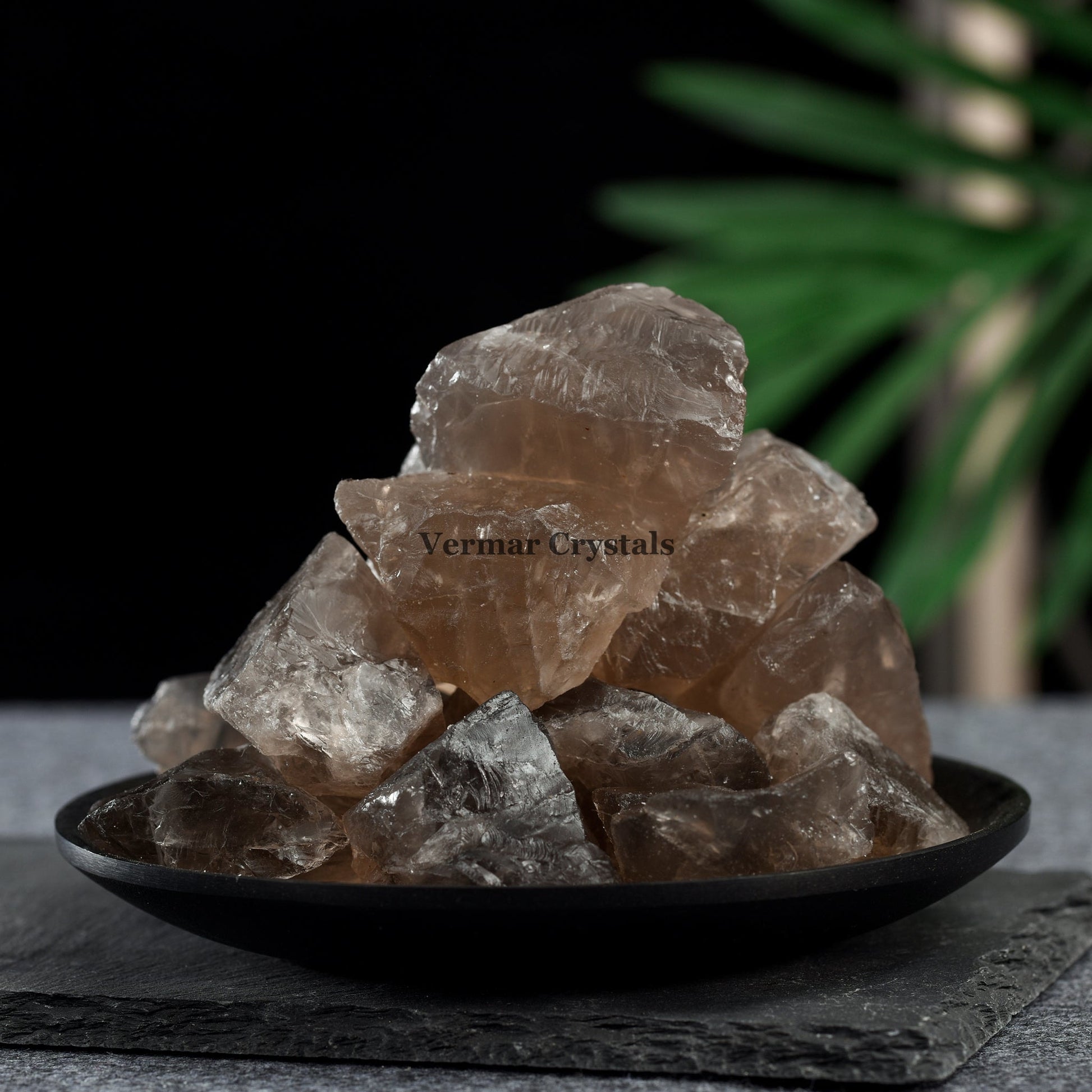 Pile of natural smoky quartz crystal stones with rough translucent brown and gray surfaces on a black plate