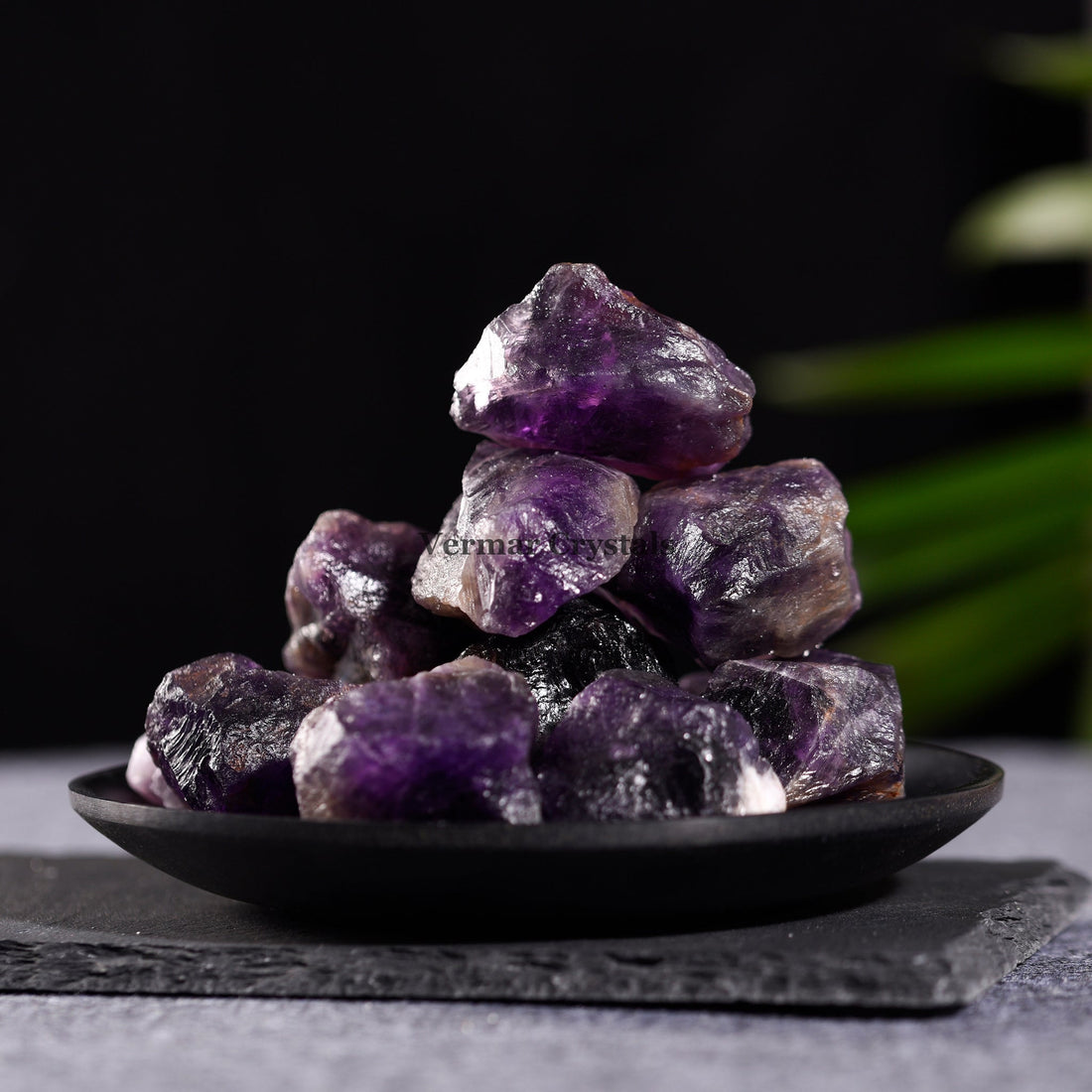 Collection of irregular natural amethyst quartz stones with purple hues displayed in a black bowl on white background