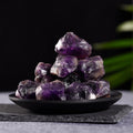 Pile of natural raw amethyst quartz crystals with purple hues displayed on a black plate against dark background