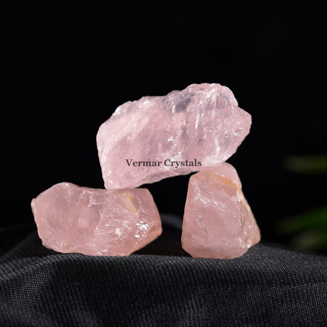 Natural rose quartz crystal stones in soft pink hues arranged on a black dish against white background