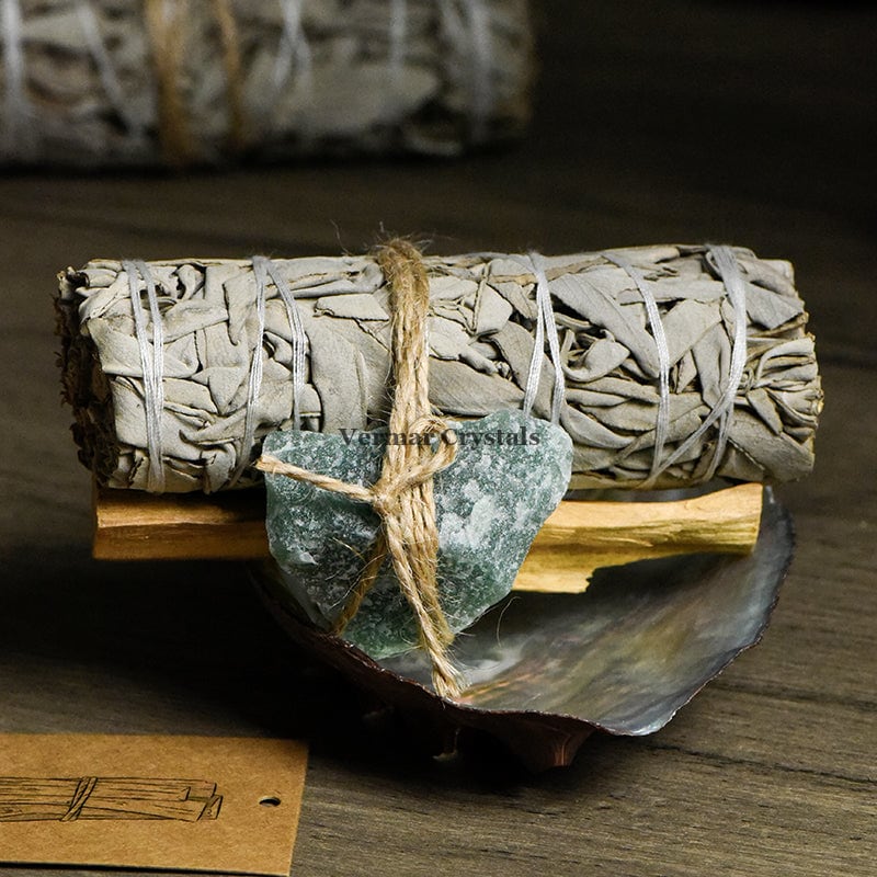 Bundle of Mexican white sage, palo santo stick, and green aventurine stone with kraft tags on wooden surface
