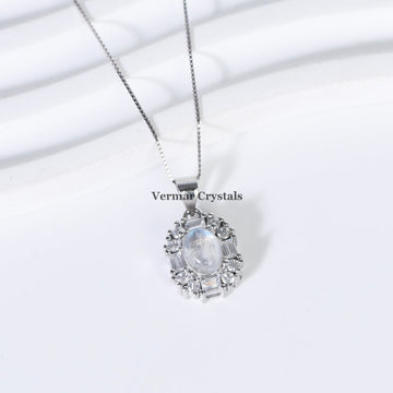 Delicate silver pendant with oval blue moonstone surrounded by clear crystals on fine chain against white background