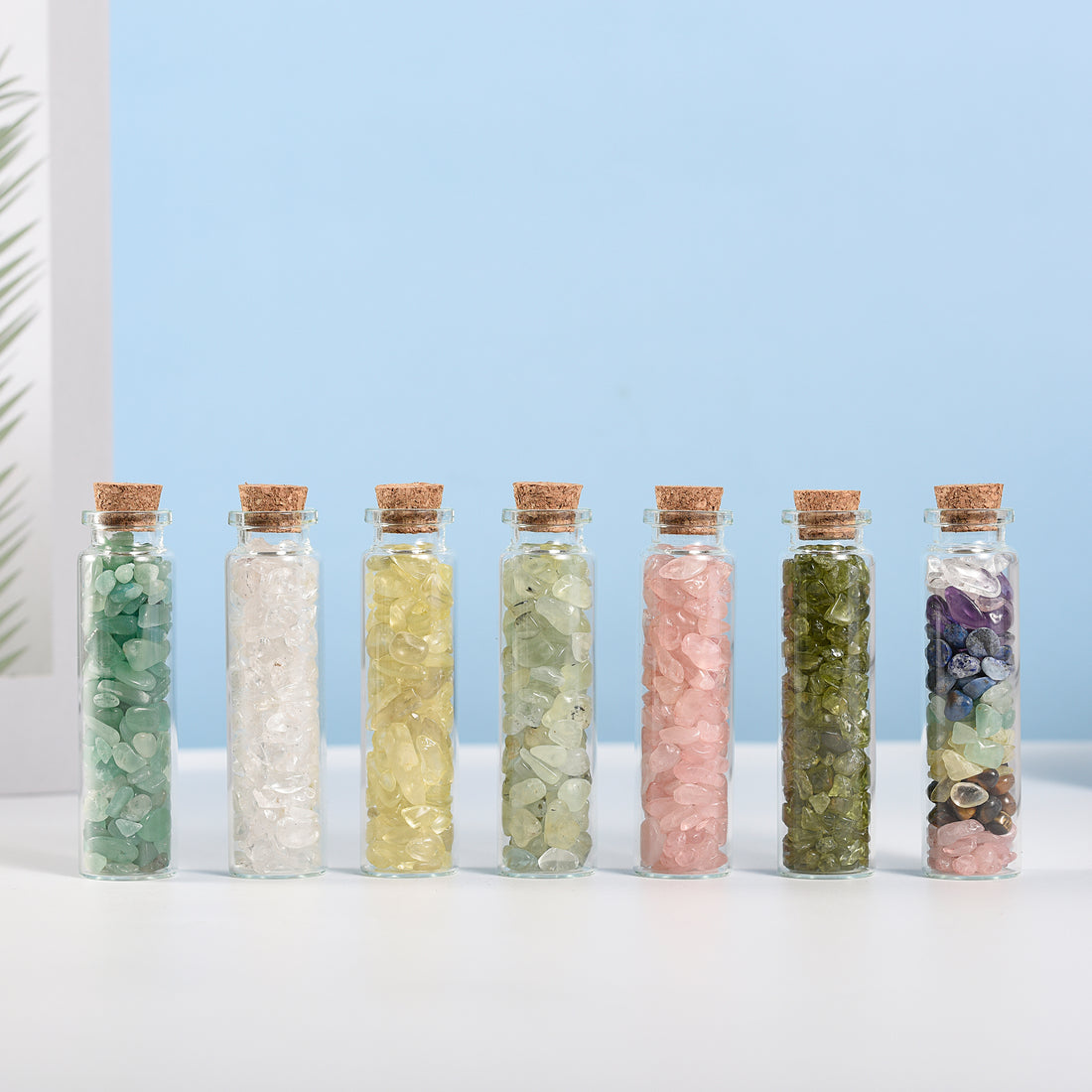 Seven small glass bottles filled with assorted natural crystal chips sealed with cork stoppers on white surface
