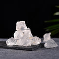 Naturally formed clear quartz crystals stacked on a dark slate surface with a black background and green leaf detail