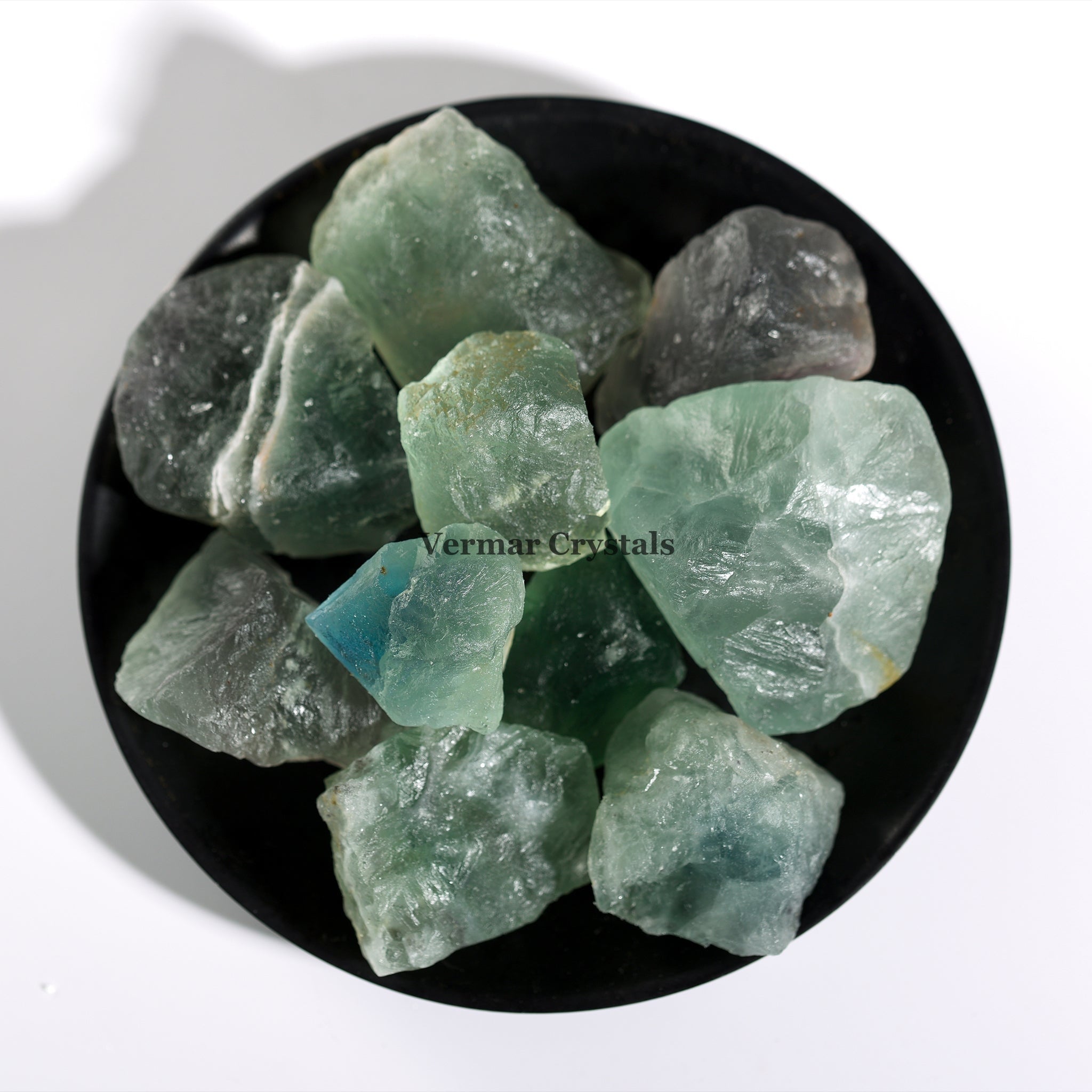 Collection of natural green fluorite crystal stones with translucent, irregular shapes displayed on a black dish