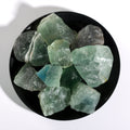 Collection of natural green fluorite crystal stones with translucent, irregular shapes displayed on a black dish