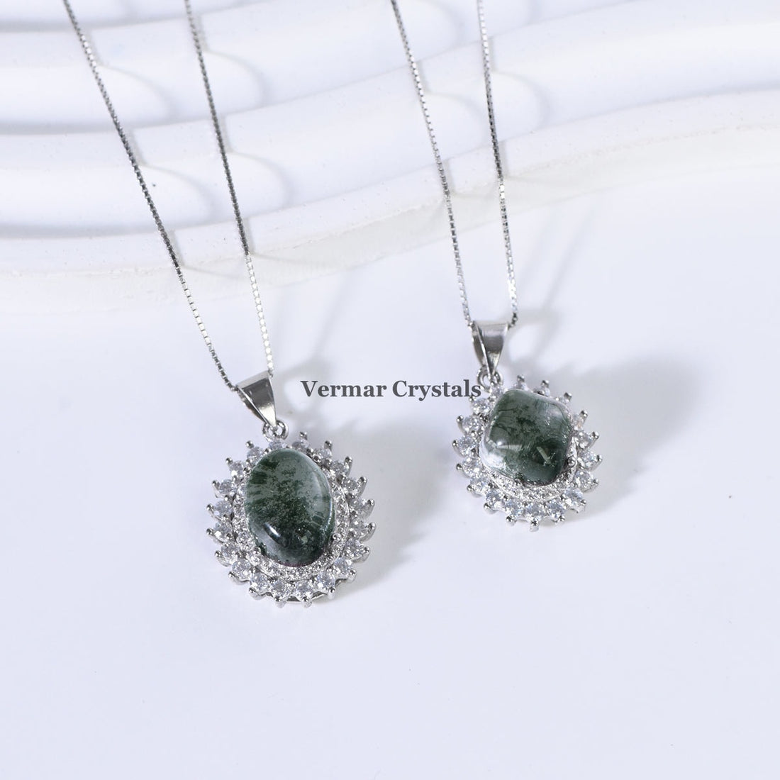 Green phantom quartz pendant necklace with silver halo setting and delicate chain displayed on white column background