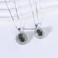 Two green phantom quartz pendants with silver halos and delicate chains on white textured surface