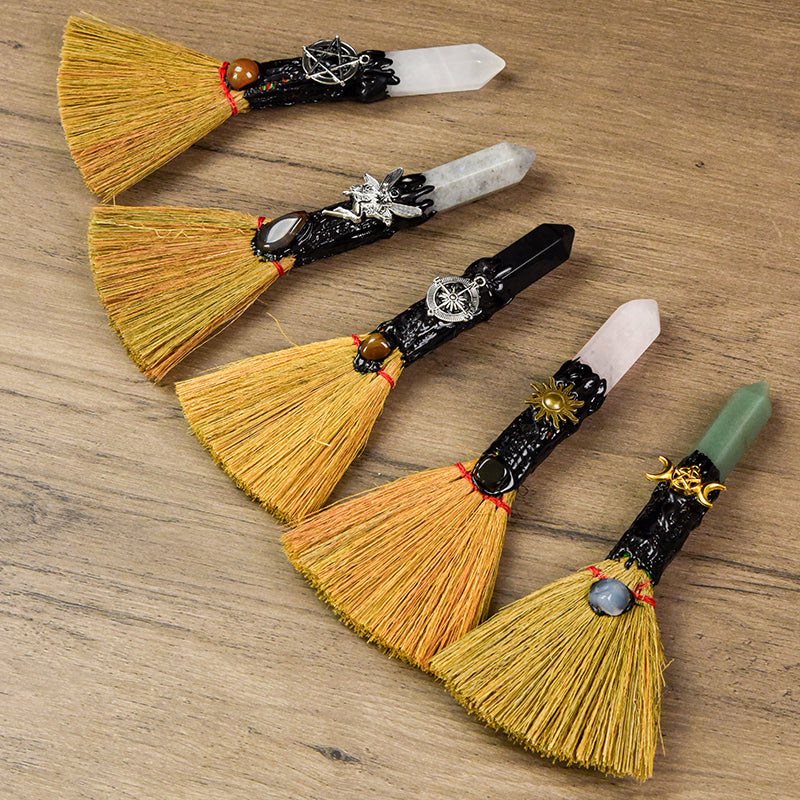 Five handcrafted mini ritual witch brooms with crystal points and symbolic charms on rustic wooden surface