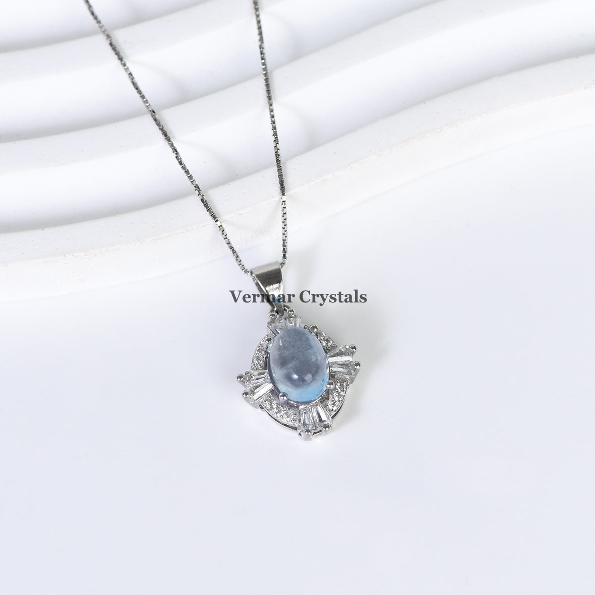 Elegant silver pendant necklace with aquamarine blue oval stone surrounded by sparkling halo stones on white background