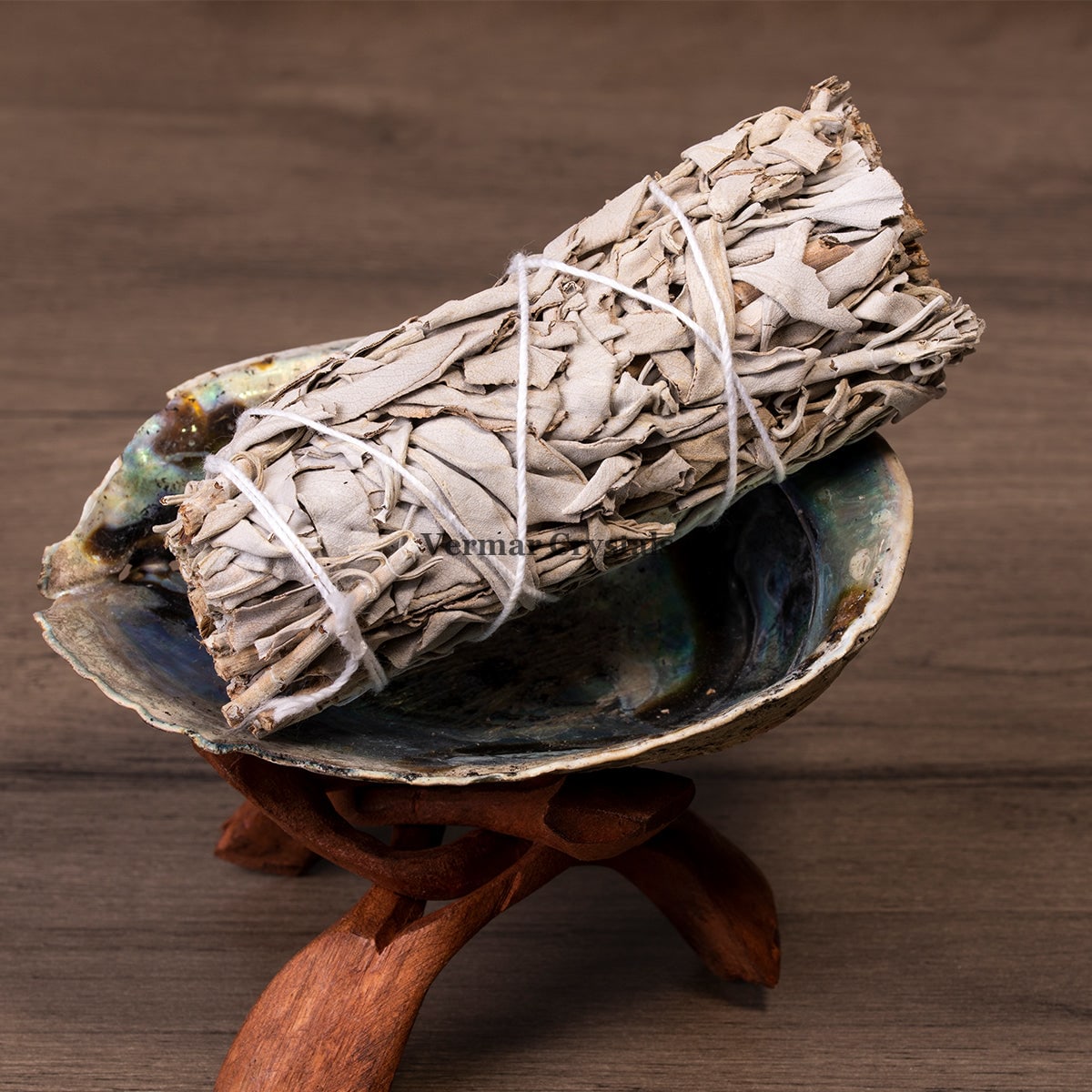 Bundle of dried white sage wrapped with white string resting in an abalone shell on wooden stand