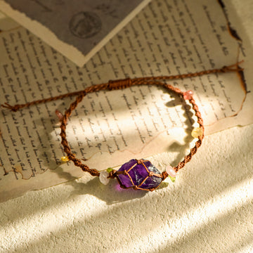 Handcrafted amethyst raw crystal wrapped in brown cord with small beads, resting on vintage handwritten letters in sunlight
