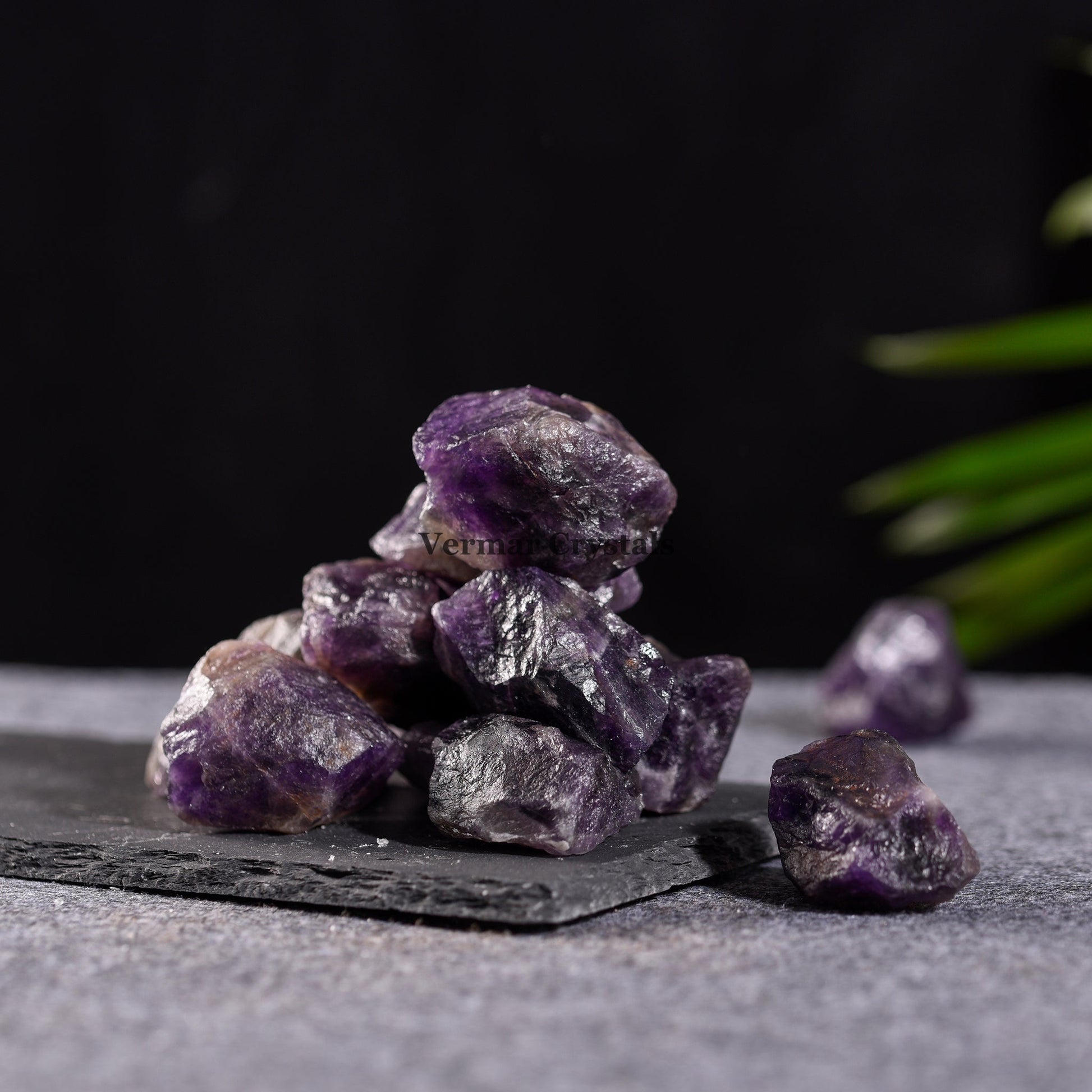 Pile of raw amethyst quartz crystal stones with deep purple hues on a dark textured surface