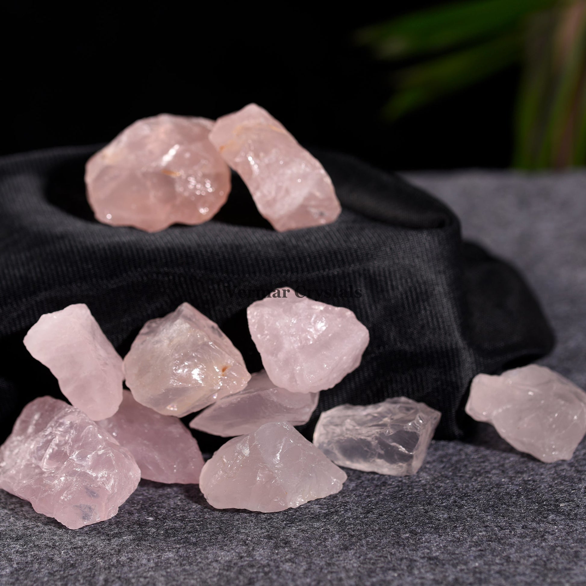 Natural rose quartz crystal stones scattered on grey surface with black pouch in soft lighting for healing energy