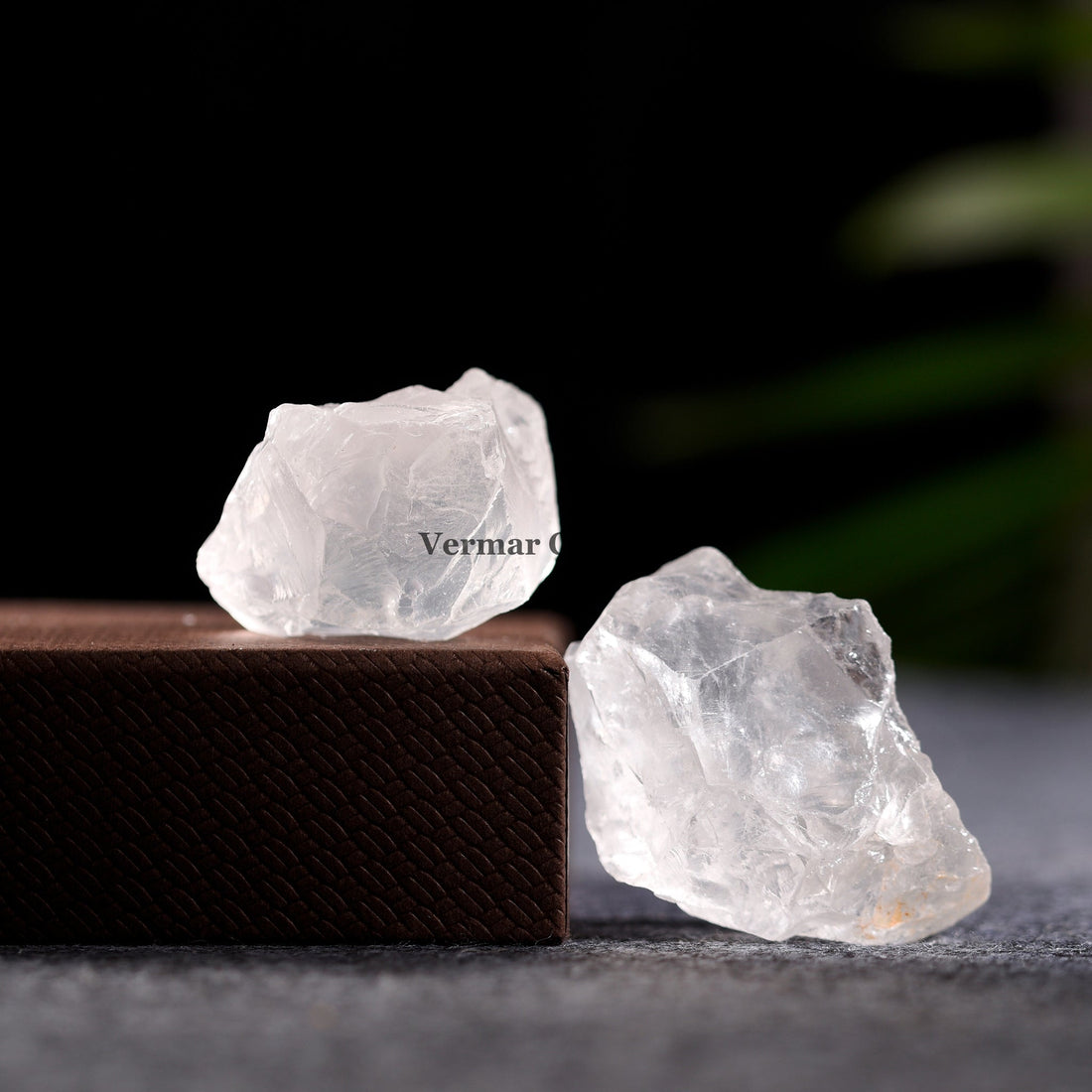 Naturally formed clear quartz crystals stacked on a dark slate surface with a black background and green leaf detail