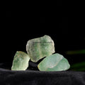 Three natural rough green fluorite crystal stones resting on black fabric with a dark background