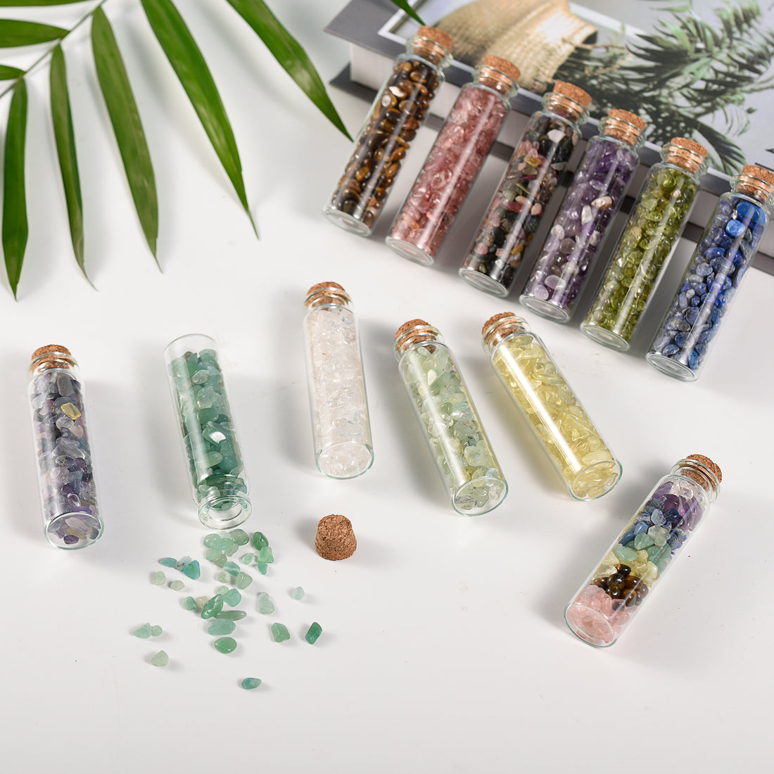 Seven small glass bottles filled with assorted natural crystal chips sealed with cork stoppers on white surface