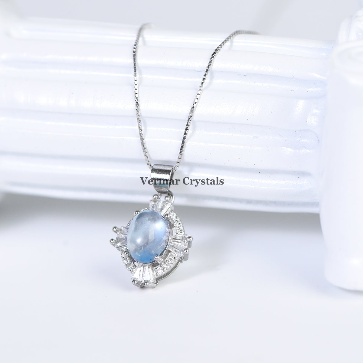 Elegant aquamarine blue oval pendant with halo of sparkling stones on delicate silver chain against white background