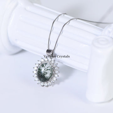 Green phantom quartz pendant necklace with silver halo setting and delicate chain displayed on white column background