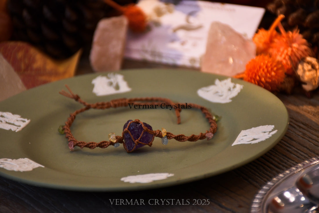Handcrafted amethyst stone wrapped with brown macrame cord, accented with small pastel beads on textured surface and paper background