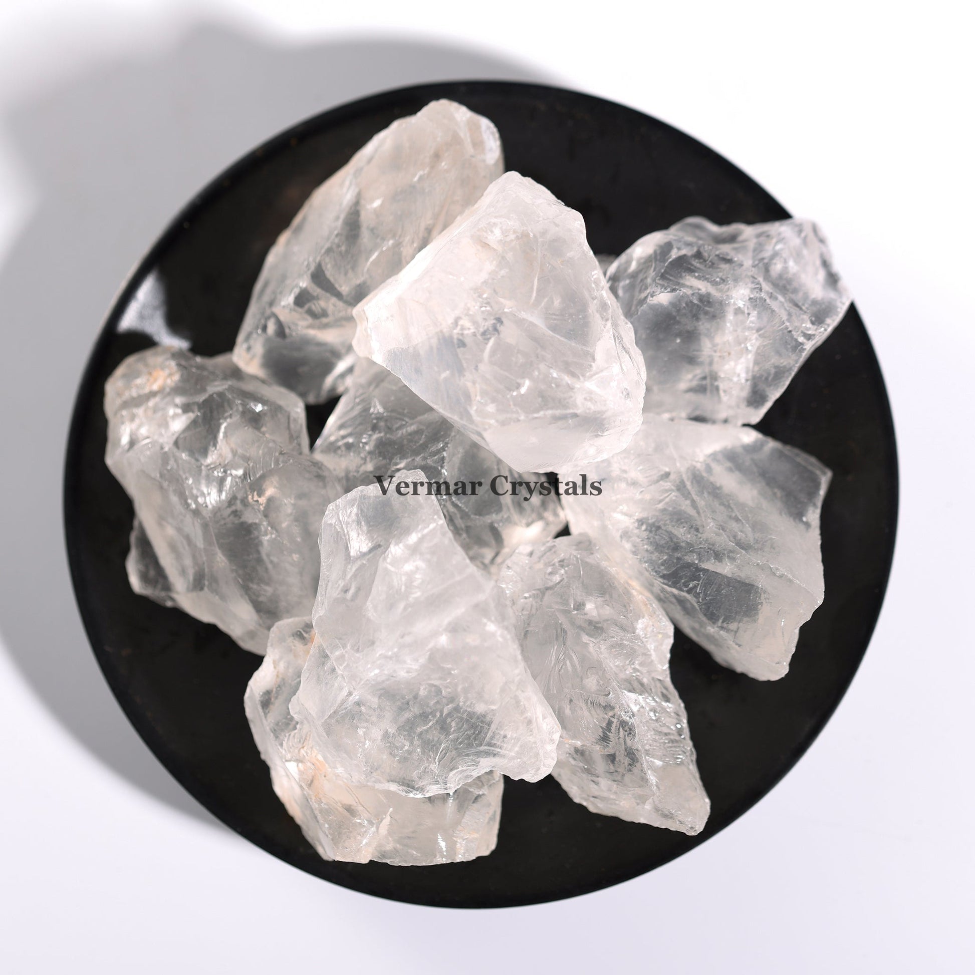 Natural clear quartz raw crystal stones arranged on a black round dish against a white background