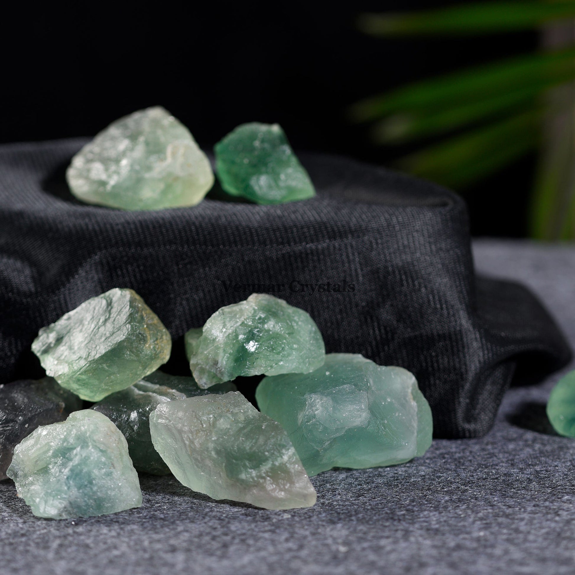 Collection of natural green fluorite crystal stones in various shapes and sizes on a gray surface with black fabric background