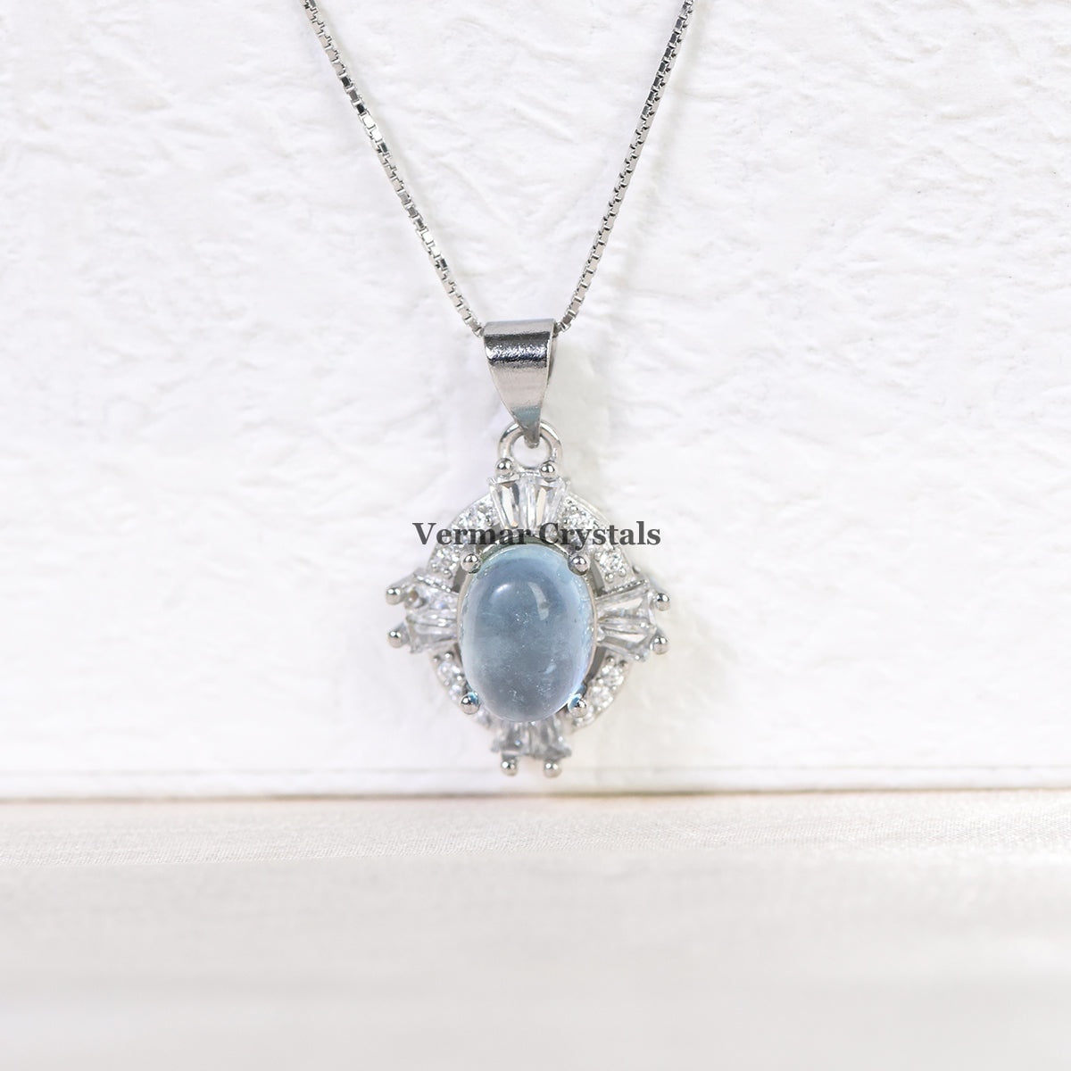 Elegant silver necklace with oval aquamarine blue pendant surrounded by sparkling stones on white background
