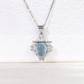 Elegant silver necklace with oval aquamarine blue pendant surrounded by sparkling stones on white background