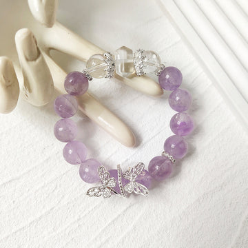 Lavender amethyst beaded bracelet with silver butterfly charms displayed on cream ceramic hand on white textured surface