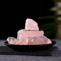 Natural rose quartz crystal stones stacked on a black dish with a dark blurred background for meditation use