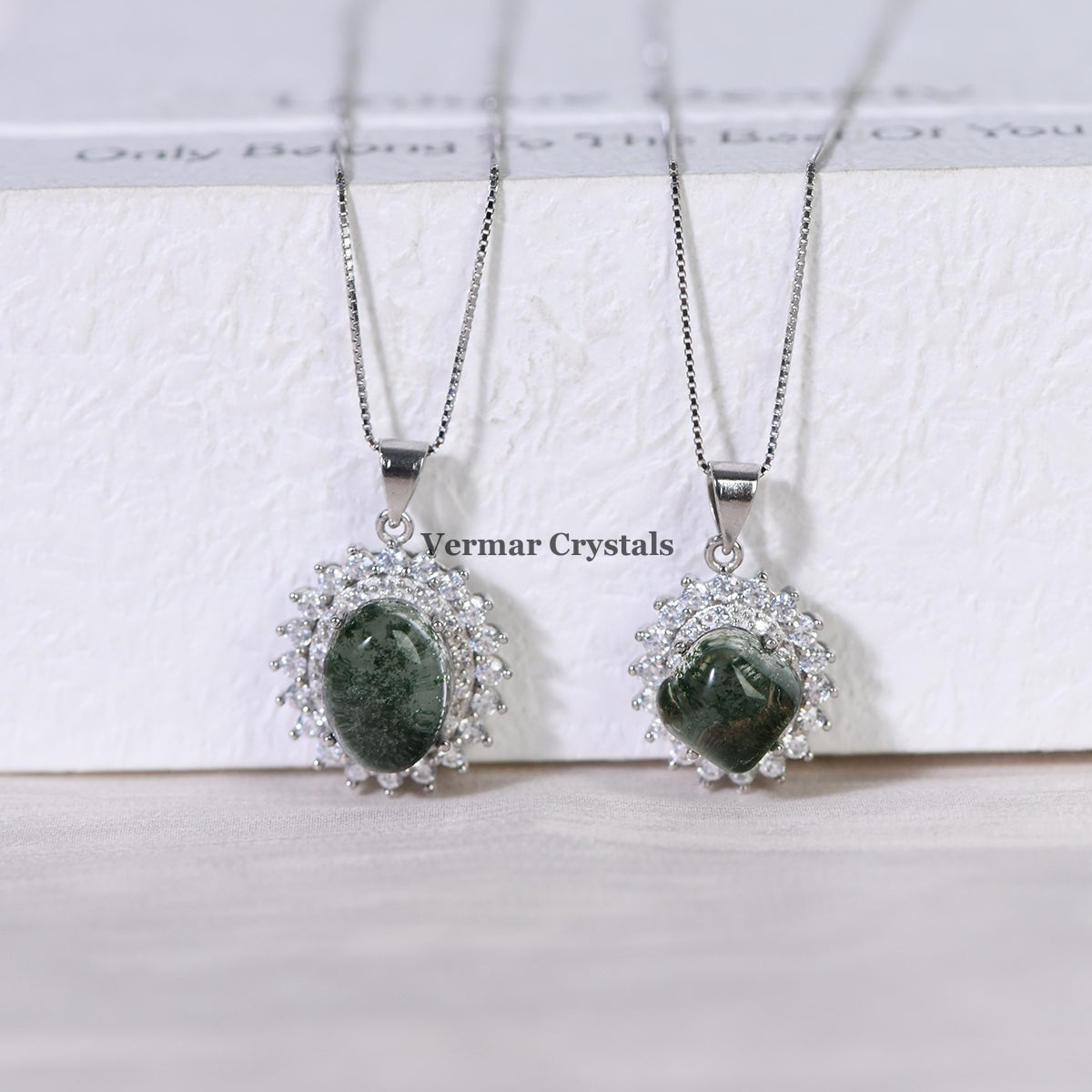 Two elegant silver necklaces with green phantom quartz stones surrounded by sparkling crystals on white surface