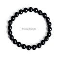 Stretchy bracelet made of polished round black obsidian crystal beads arranged in a circle on white background