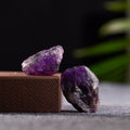 Two natural raw amethyst quartz stones with deep purple hues against a dark and textured background