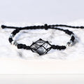 Handcrafted Herkimer Diamond crystal bracelet with braided black cord and silver beads resting on a white textured surface