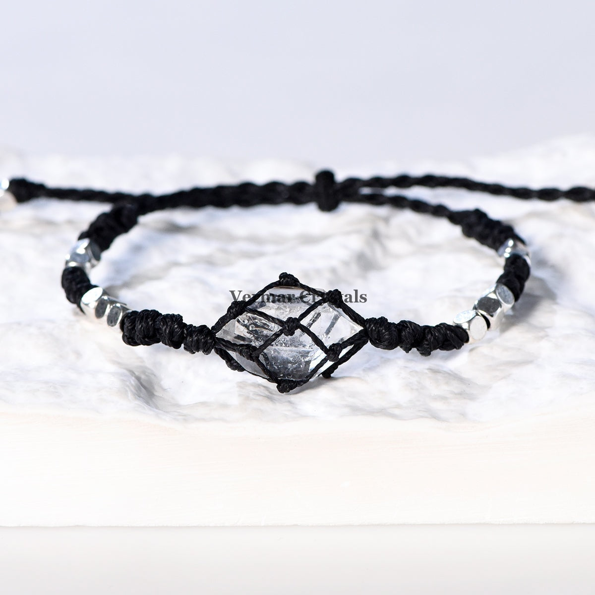 Handcrafted Herkimer Diamond crystal bracelet with braided black cord and silver beads resting on a white textured surface