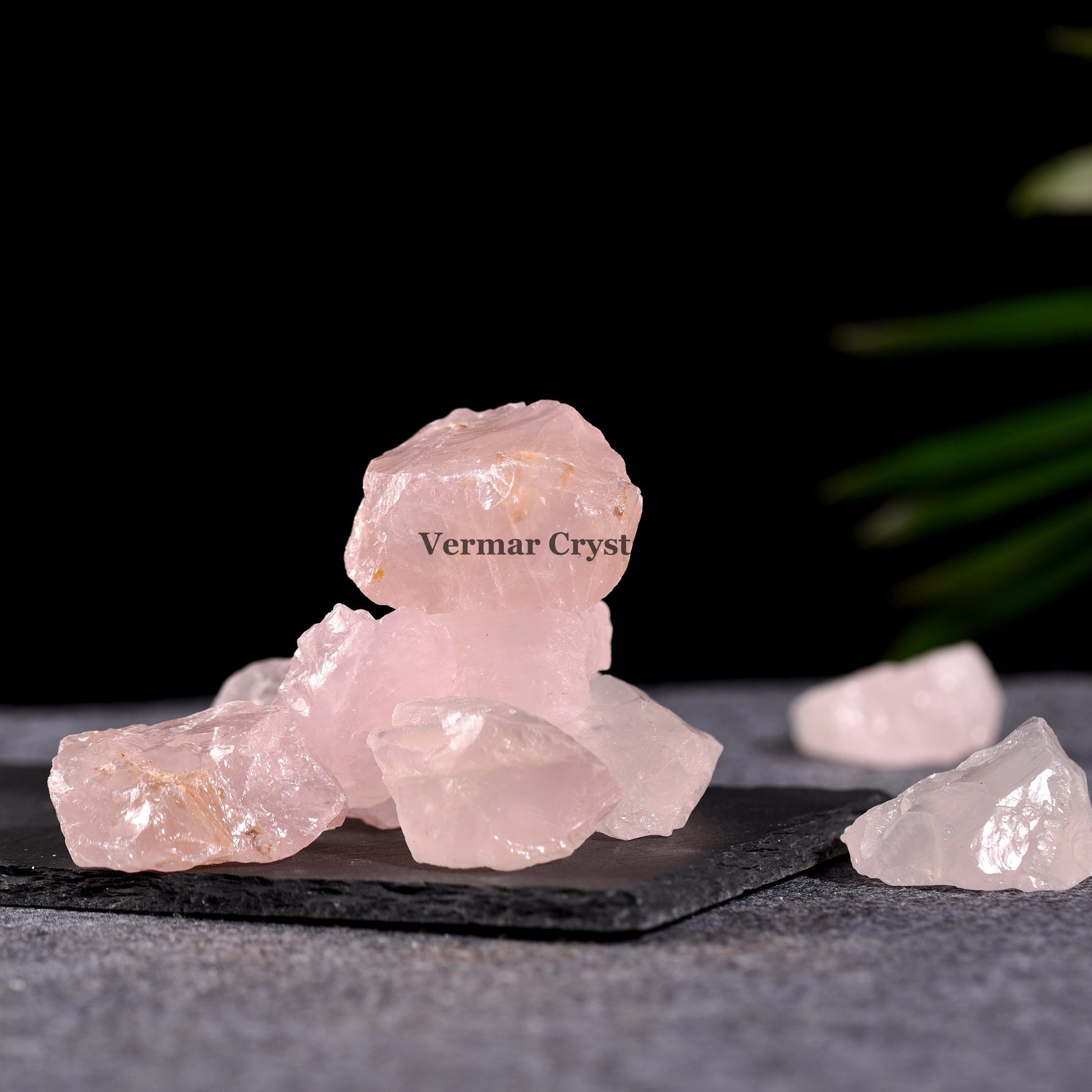 Natural rose quartz crystal stones with soft pink hues displayed on a dark stone slab against black background