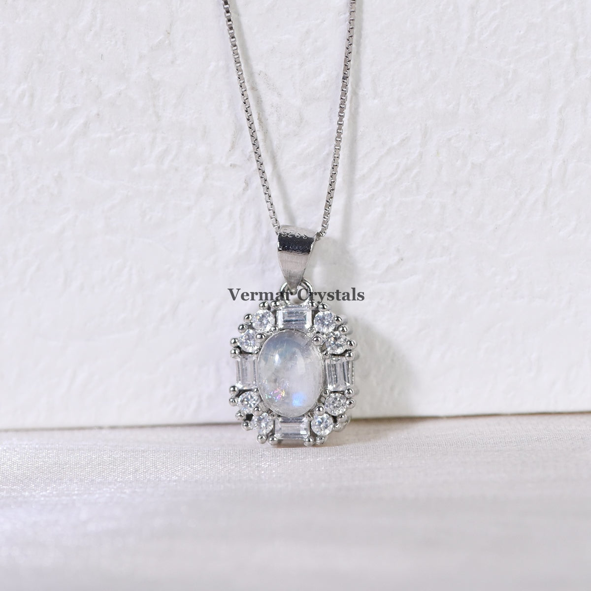 Silver pendant necklace featuring an oval blue moonstone surrounded by sparkling crystal accents on white background