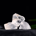 Three naturally formed clear quartz stones resting on black fabric against a dark background