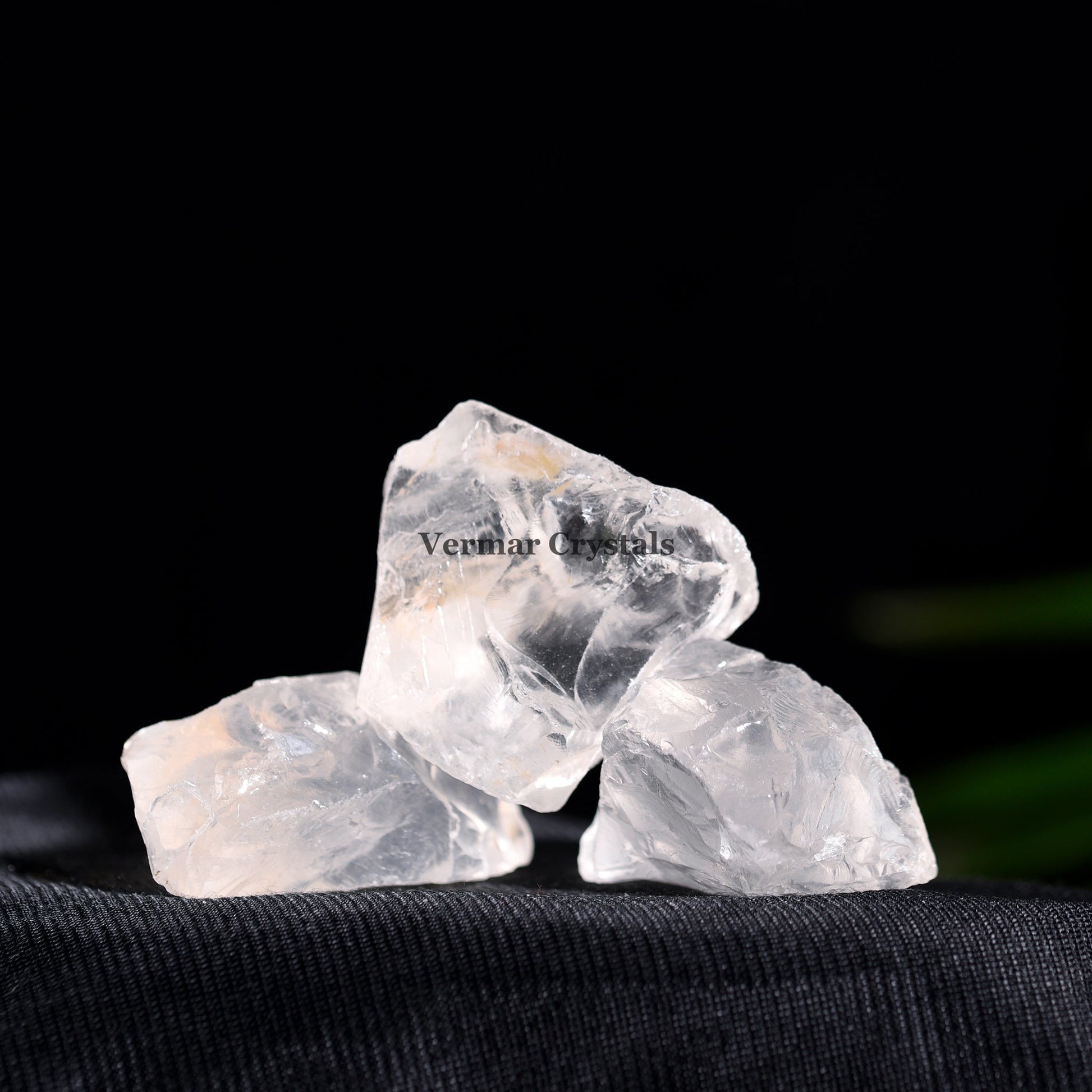 Three naturally formed clear quartz stones resting on black fabric against a dark background