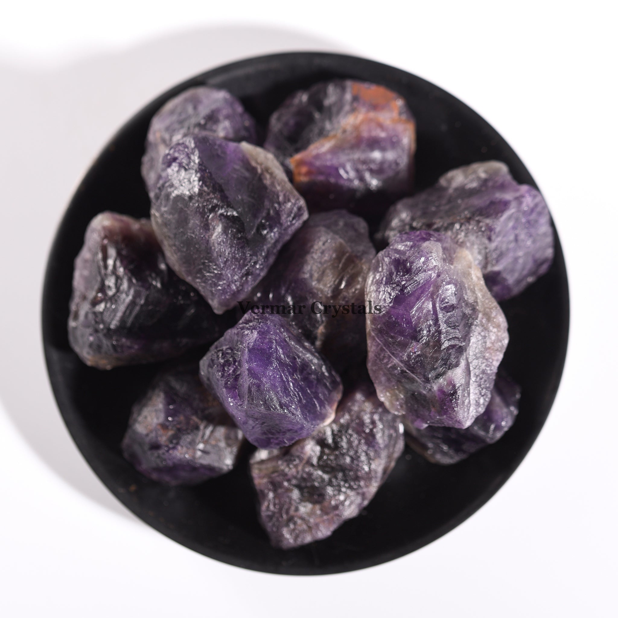 Collection of irregular natural amethyst quartz stones with purple hues displayed in a black bowl on white background