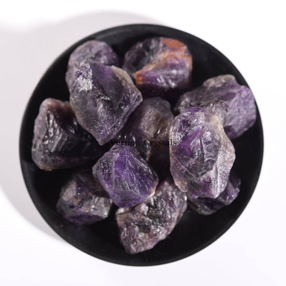 Collection of irregular natural amethyst quartz stones with purple hues displayed in a black bowl on white background
