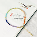 Faceted gemstone seven chakra bracelet with multicolored beads and gold accents resting on an open book page