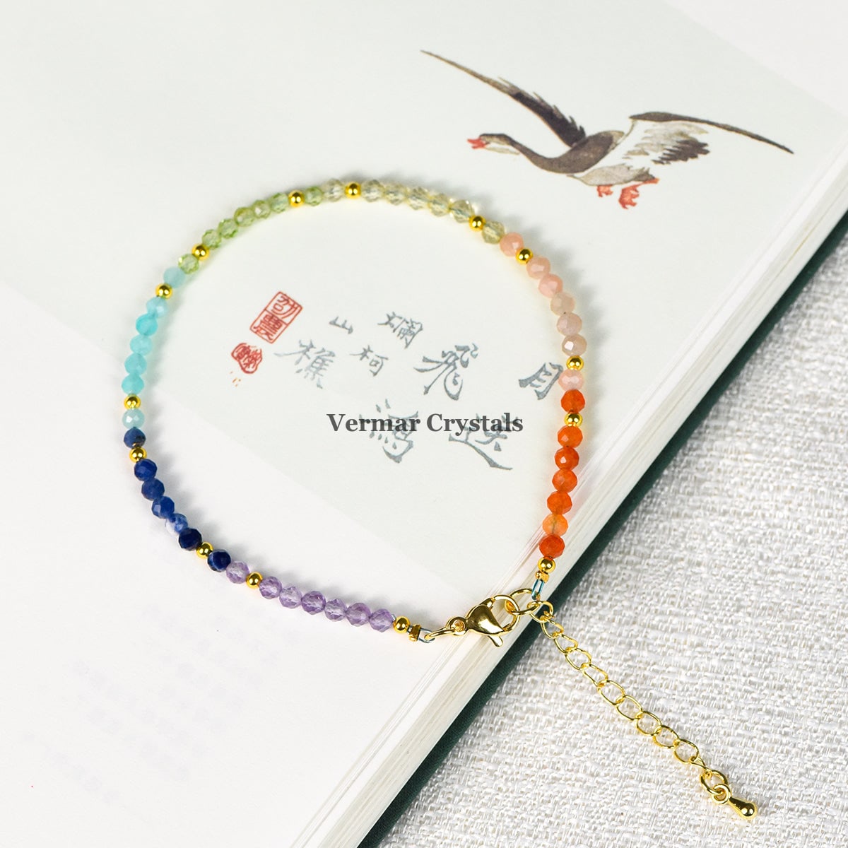 Faceted gemstone seven chakra bracelet with multicolored beads and gold accents resting on an open book page