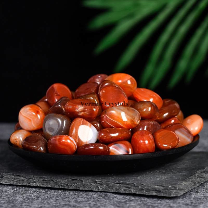 Pile of polished red agate tumblestones with varying shades of red and white on a black plate background