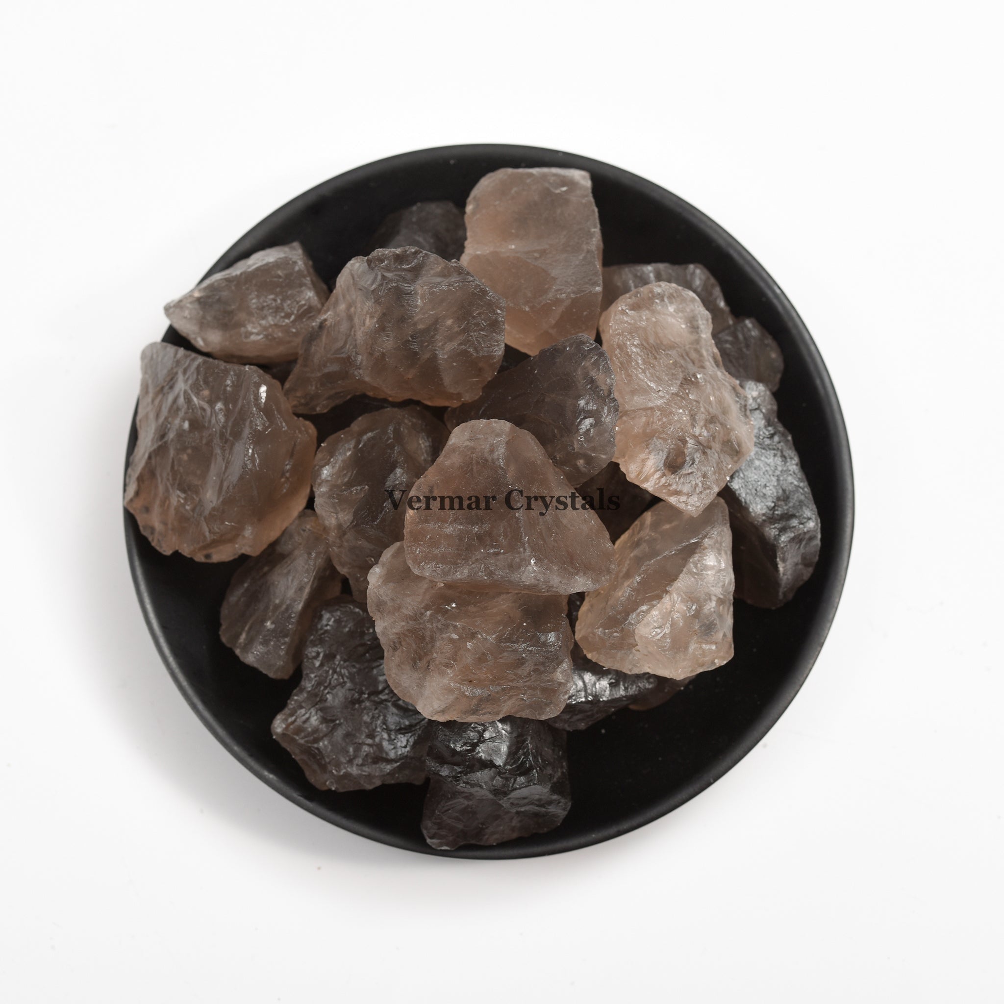 Natural smoky quartz crystal stones in varying shades of brown and gray arranged in a black dish on white background