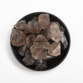 Natural smoky quartz crystal stones in varying shades of brown and gray arranged in a black dish on white background
